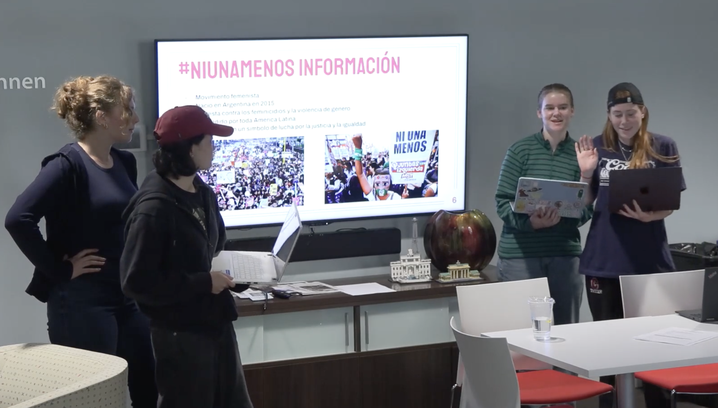 Four people stand around a TV screen with three of them holding laptops and one reading from the laptop